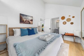 A bedroom with a bed, pillows, a blanket, a painting, and wall decor. - Harbor Home - Walking Distance to Twin Lakes Beach! (Santa Cruz)