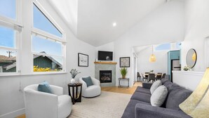 A living room with a fireplace, a TV, and a dining area in the background. - Harbor Home - Walking Distance to Twin Lakes Beach! (Santa Cruz)