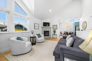 A living room with a fireplace, a TV, and a dining area in the background. - Harbor Home - Walking Distance to Twin Lakes Beach! (Santa Cruz)