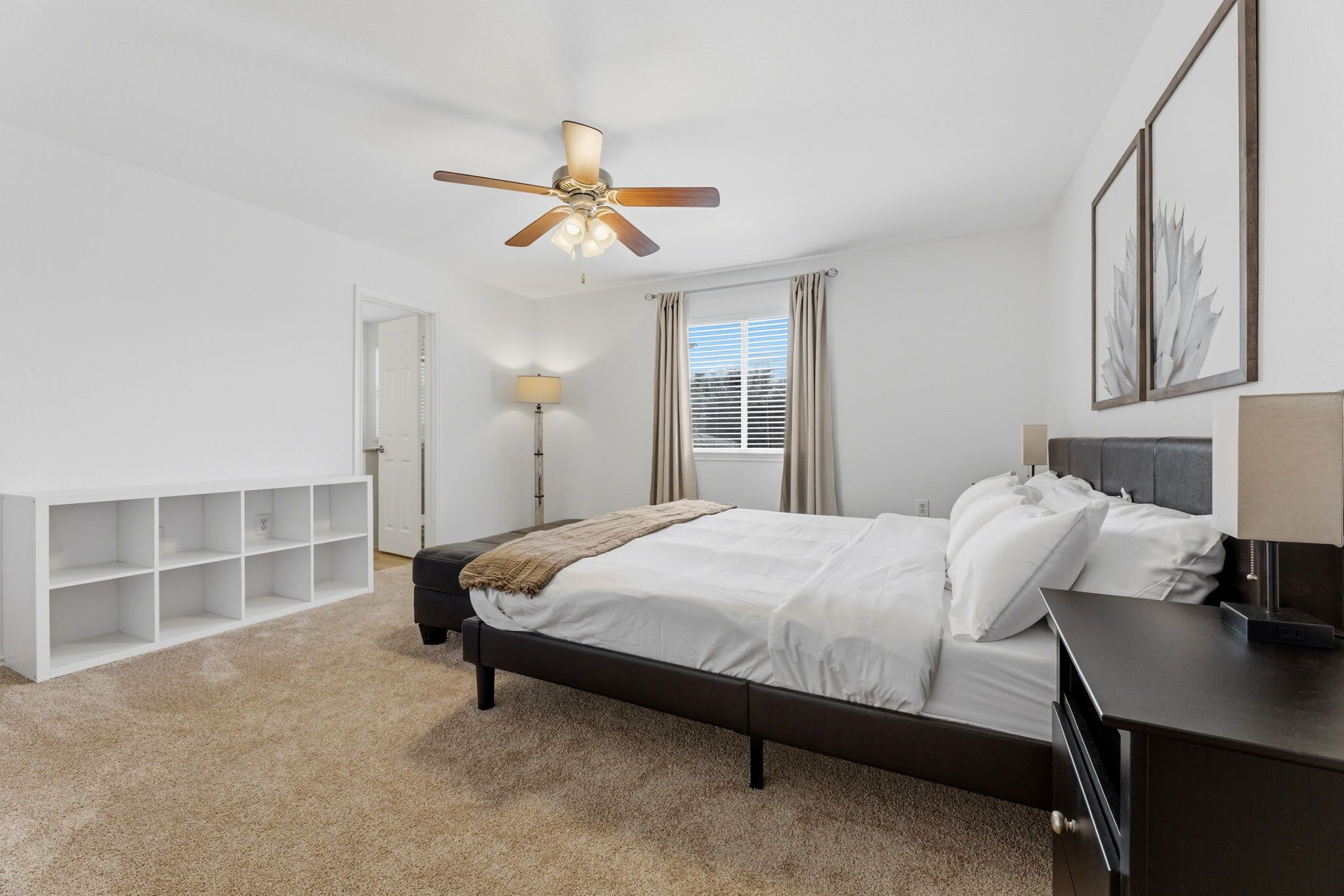 A bedroom with a bed, a desk, a chair, a ceiling fan, a window with curtains, and a bookshelf.
