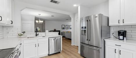Une cuisine moderne avec des meubles blancs, des appareils électroménagers en acier inoxydable et un plancher en bois.