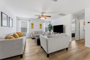 Ein modernes Wohnzimmer mit Deckenventilator, Flachbildfernseher und einer Sofagarnitur.