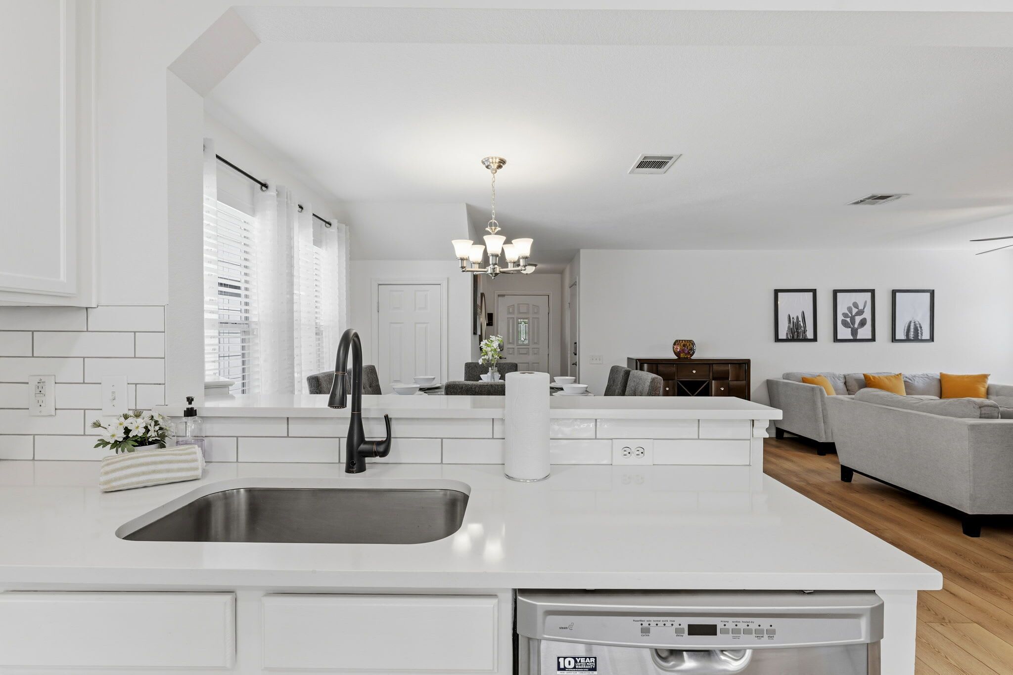 A modern kitchen with a central island, a built-in dishwasher, and a large window with blinds.