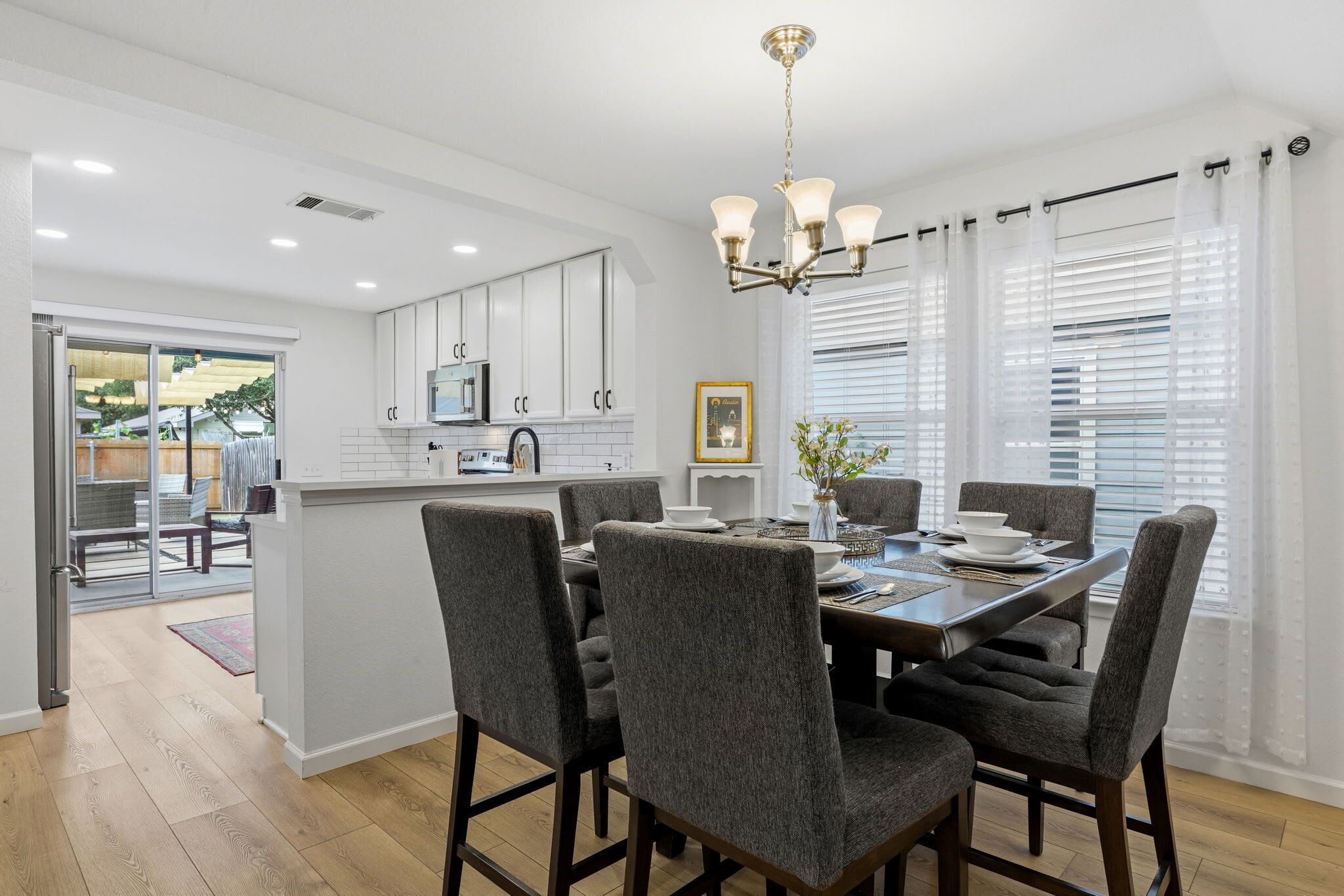 A modern kitchen with white cabinets, a central island, and a dining area with grey upholstered chairs.