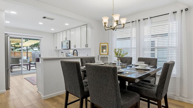 Una cocina moderna con armarios blancos, una isla central y un comedor con sillas tapizadas en gris.