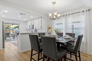 A modern kitchen with white cabinets, a central island, and a dining area with grey upholstered chairs. - Cowboy Pool, Fire Pit & Putt Putt Near DT For 10! (Austin)
