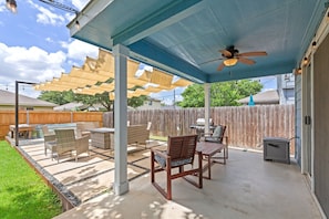 Eine überdachte Terrasse mit Gartenmöbeln, einem Deckenventilator und einem Holzzaun im Hintergrund.