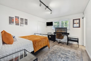 Ein Schlafzimmer mit Bett, Schreibtisch, Fernseher und einem Fenster mit Jalousien.