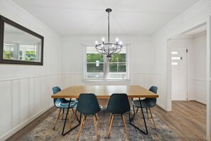 Ein Esszimmer mit Holztisch, vier Stühlen, einer Kronleuchter und einem großen Spiegel an der Wand.
