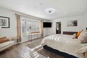 Ein Schlafzimmer mit einem Bett, einer Couch, einem Fernseher und einem Fenster mit Jalousien.