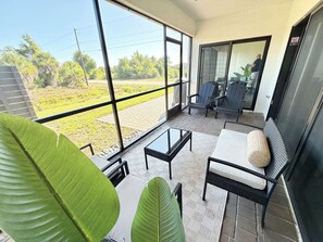 Ein Balkon mit Glastür, Tisch, Stühlen und großen Grünpflanzen.
