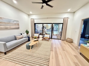 Ein modernes Wohnzimmer mit Sofa, Couchtisch und Sesseln, einem großen Gemälde an der Wand und einer Glasschiebetür zu einem Außenbereich.