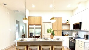 A modern kitchen with a central island, wooden cabinets, stainless steel appliances, and a potted plant. - Sea Salt Cottages AC • Two Luxury Villas • Sleeps 12 next Boca grande Beach (Port Charlotte)