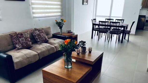 A modern living room with a sofa, coffee table, and dining area.