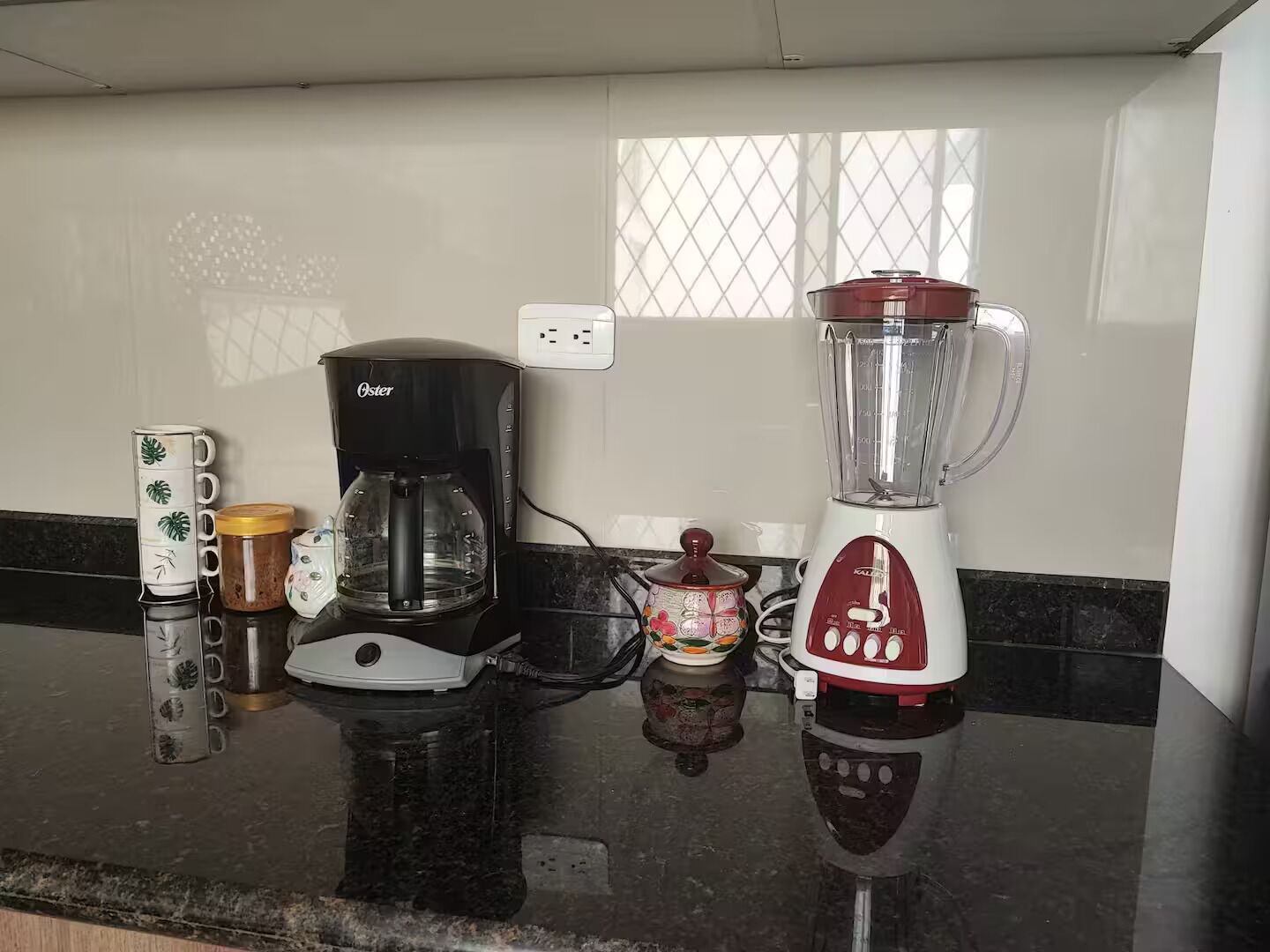 Uma bancada de cozinha com uma cafeteira, um liquidificador e uma caneca decorativa.