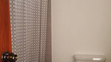 A bathroom with a toilet, a trash bin, a patterned shower curtain, and a wooden door.
