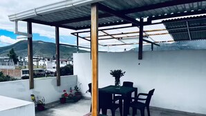 A rooftop patio with a table and chairs, a wooden post, and potted plants.