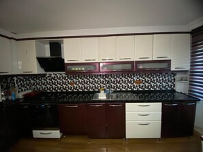 A kitchen with white and maroon cabinets, a black countertop, and a tiled backsplash.