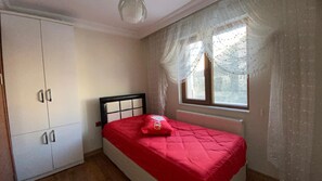 A bedroom with a bed, a wardrobe, and a window with curtains.