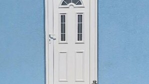 A white door with a small window above it, set against a blue wall.
