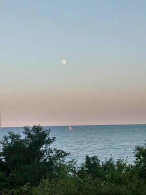 A coastal scene with a sailboat on the water and a moon in the sky.