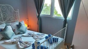 A single bed with a metal frame, a headboard, and blue bedding. There is a window with curtains, and the room has wooden flooring.