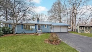 Une maison de plain-pied avec un garage, une pelouse devant et des arbres sans feuilles en arrière-plan.