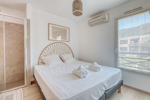 Ein Schlafzimmer mit Bett, Dusche, einem gerahmten Bild, einer Klimaanlage und einem Fenster.