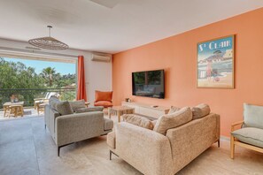 Ein modernes Wohnzimmer mit Fernseher, bequemer Sitzgelegenheit, einem Balkon mit Blick und einem Poster an der Wand.