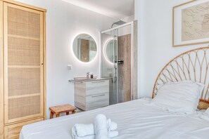 A bedroom with a bed, a wooden wardrobe, a bathroom with a shower, and a round mirror. - Luxury 3-bedroom apartment, 350 m from Saint-Clair beach (Le Lavandou)