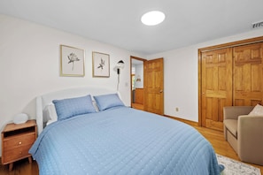 Quarto com cama, mesa de cabeceira, cadeira e portas de madeira.