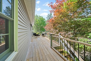 A wooden deck with outdoor furniture, a railing, and a view of trees and a building. - Lake Views • Private Beach • Fire Pit • Game Barn (Naples)