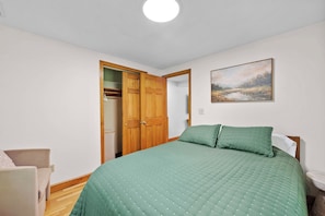 A bedroom with a bed, a wooden wardrobe, a painting on the wall, and a small bedside table. - Lake Views • Private Beach • Fire Pit • Game Barn (Naples)