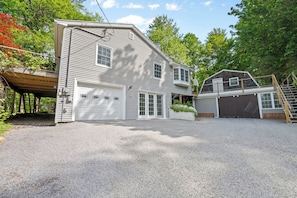 A two-story house with a garage, a covered porch, and a wooden deck. - Lake Views • Private Beach • Fire Pit • Game Barn (Naples)