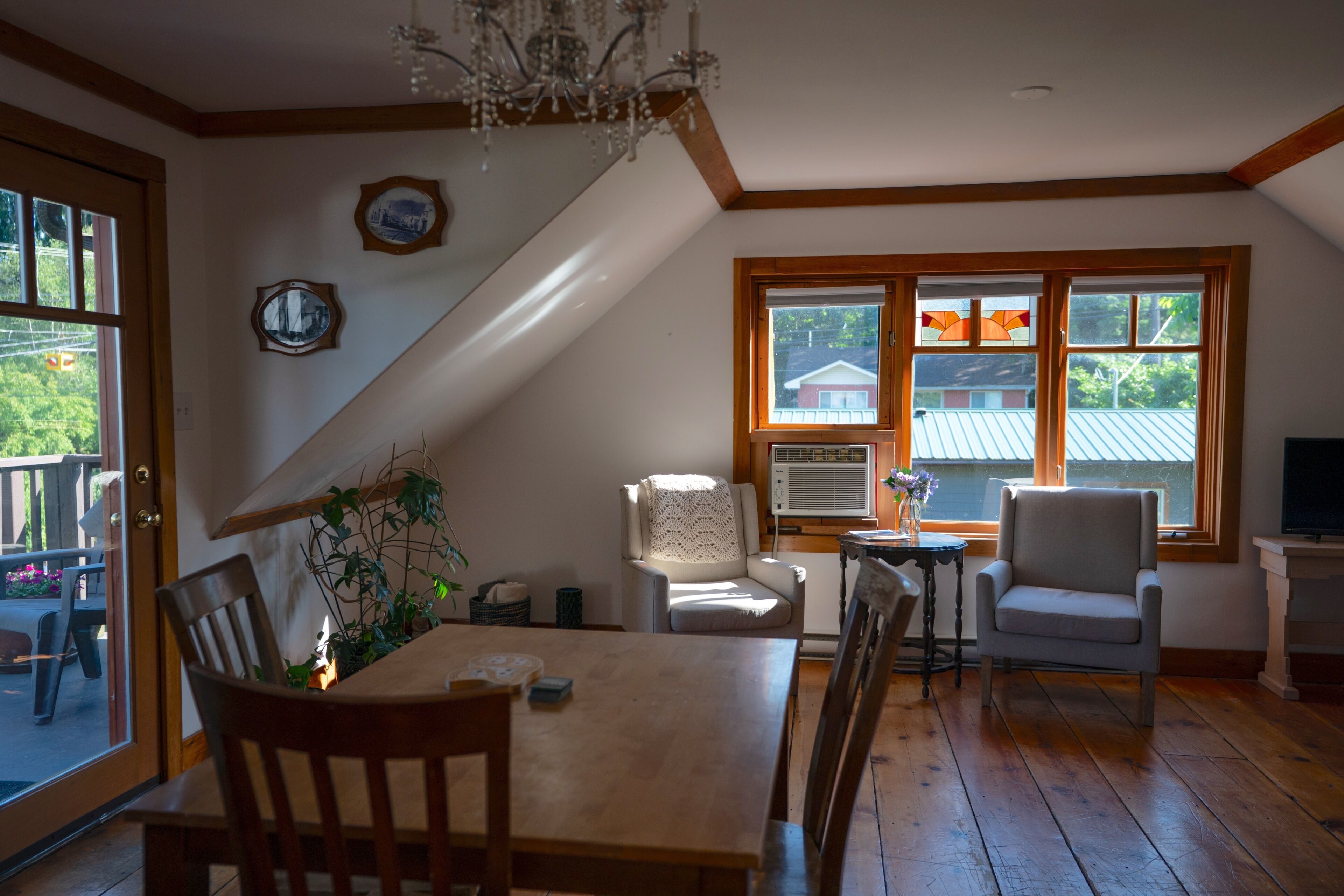 Un comedor con mesa y sillas de madera, una araña y vistas al exterior a través de amplios ventanales.