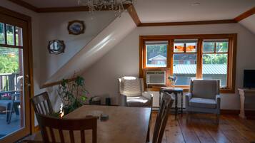 Un comedor con mesa y sillas de madera, una araña y vistas al exterior a través de amplios ventanales.
