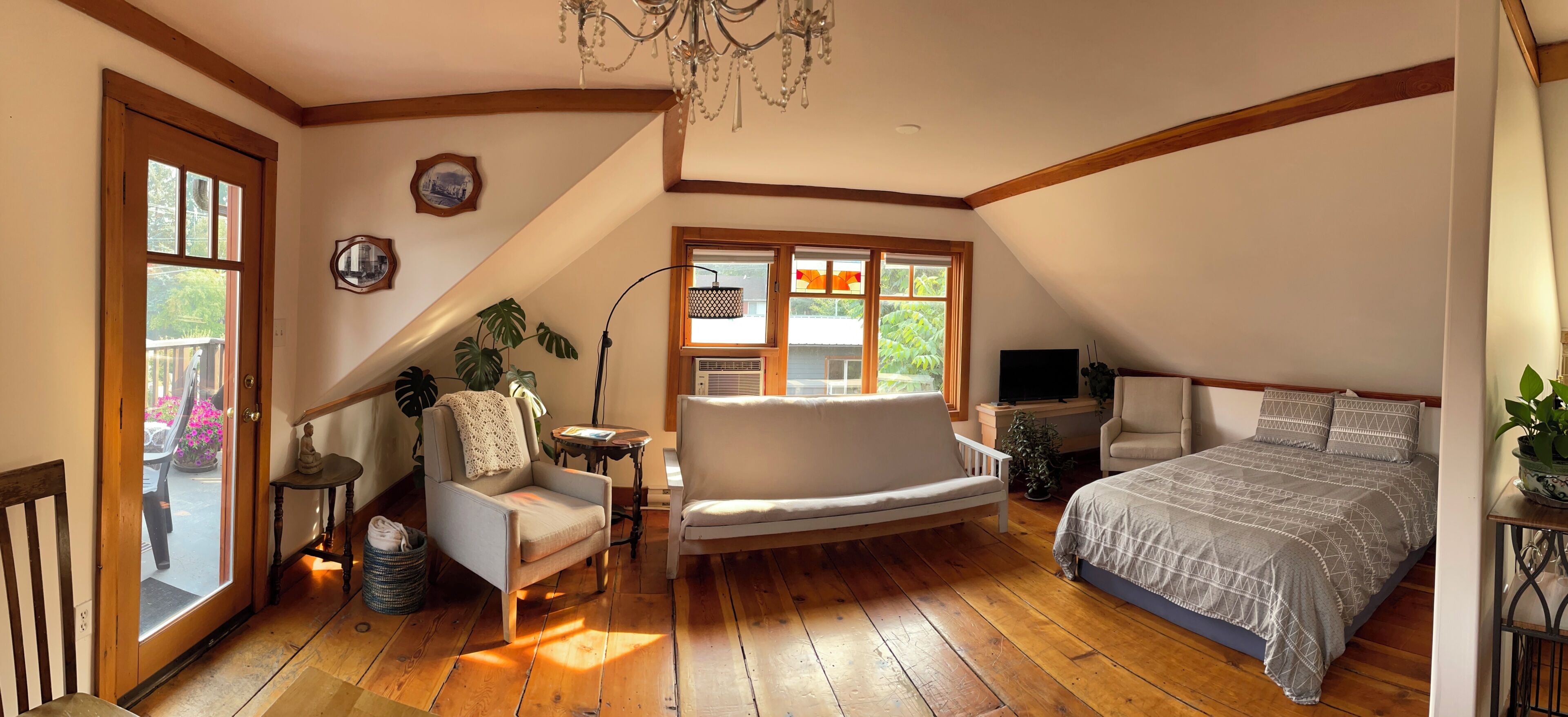 Une chambre avec un plafond en pente, un plancher en bois, un lit recouvert d’une couvre-lit à motifs, une chaise, une petite table avec une lampe et un téléviseur.