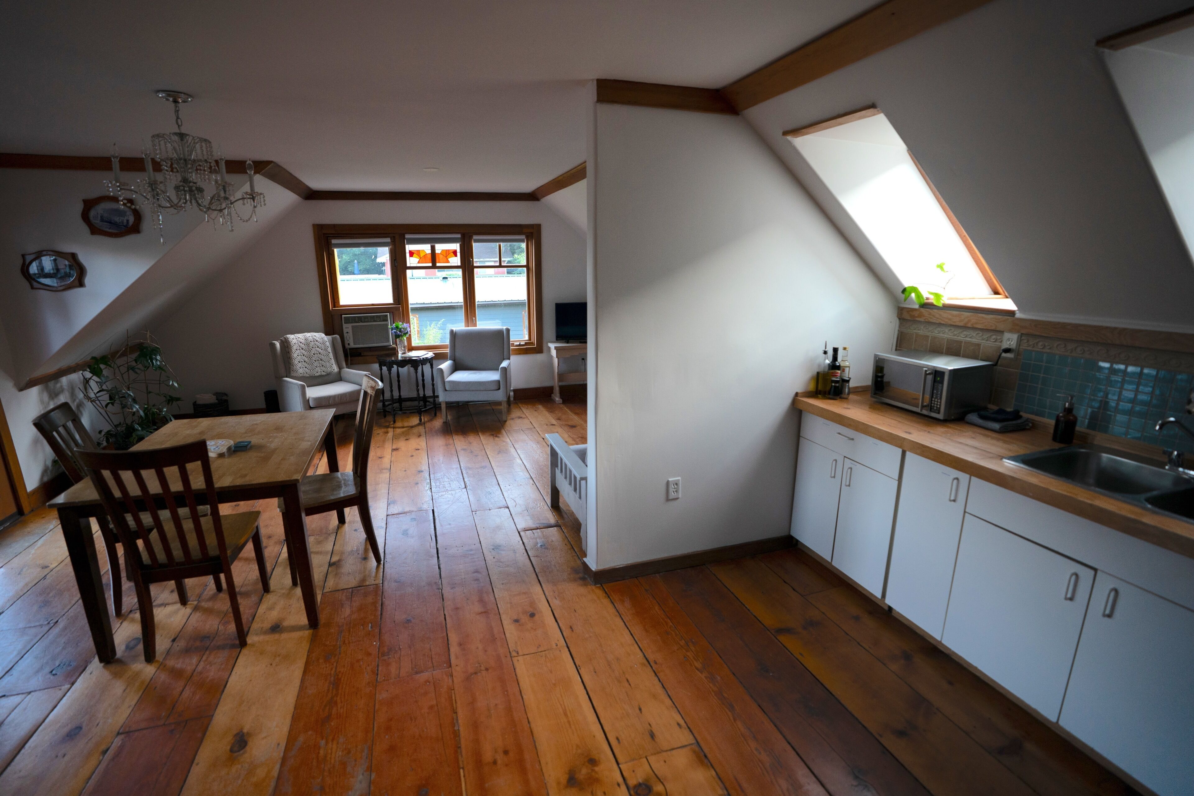 Une cuisine avec un plancher en bois, un coin repas avec une table et des chaises, un lustre et une fenêtre donnant sur un beau paysage.