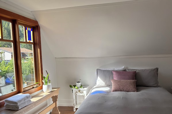 A bedroom with a bed, pillows, a nightstand, a window with curtains, and a view of the outside.
