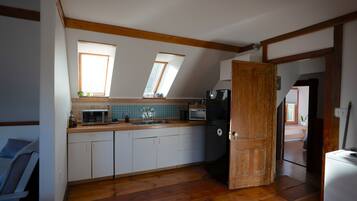 A compact kitchen with a wooden floor, white cabinets, a microwave, a toaster, and a refrigerator. There are two skylights providing natural light.