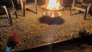 Ein Feuerkorb mit Flammen, umgeben von Stühlen und einem Kiesbereich.