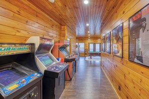 Eine Reihe von Spielautomaten in einem Raum mit Holzboden, einem Billardtisch und gerahmten Postern an der Wand.