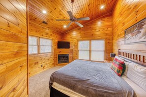 A log cabin room with a bed, a fireplace, a ceiling fan, and a television. - Newly Remodeled 4BR Suites Gatlinburg Cabin, Hot Tub & Theater Room (Gatlinburg)