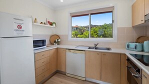 A compact kitchen with a microwave, dishwasher, and toaster. A window offers a view of greenery. - Salt on Sapphire - steps away from Campbells Beach (Sapphire Beach)