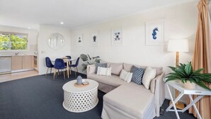 A modern living room with a sofa, a round coffee table, a dining area with chairs, and a kitchen visible through an open door. - Salt on Sapphire - steps away from Campbells Beach (Sapphire Beach)