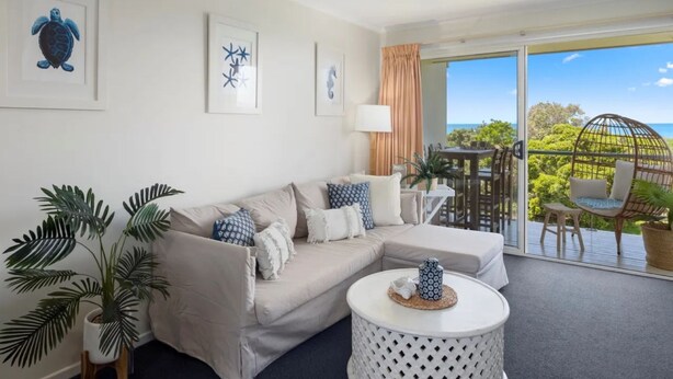 A modern living room with a beige sofa, a round coffee table, and a balcony with a view of the ocean. - Salt on Sapphire - steps away from Campbells Beach (Sapphire Beach)