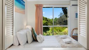 A bedroom with a bed, pillows, a window with a view of greenery, and a door. - Salt on Sapphire - steps away from Campbells Beach (Sapphire Beach)