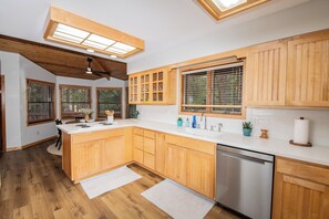 Eine moderne Küche mit Holzausstattung, einem Edelstahl-Geschirrspüler und einer großen Kücheninsel mit Spüle.