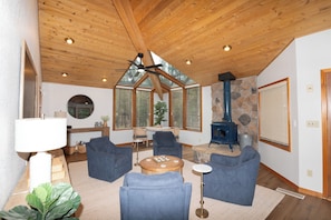Ein geräumiges Wohnzimmer mit hoher Decke, einem Steinkamin und einem großen Fenster mit Jalousien.