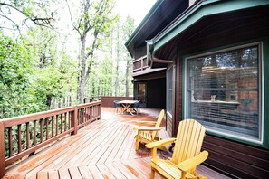 Une terrasse en bois, avec des chaises et une table, entourée d’arbres.